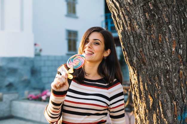 Girl with colorful lollipop next to tree