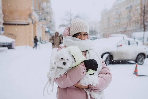 Free photo girl with a dog in her arms while snow is falling