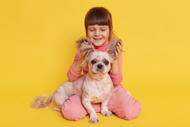 Free Photo girl with dog playing together lifts ears of puppy and laughing on yellow