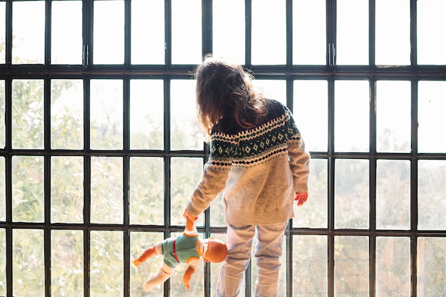 Free Photo girl with a doll looking through window