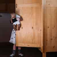 Free photo girl with doll standing behind wooden cupboard