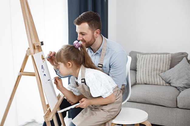 Girl with Down syndrome and her father painting on an easel with brushes