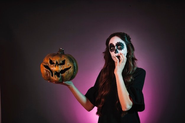 Girl with halloween makeup holding pumpkin