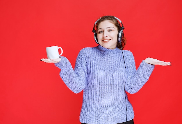 Free Photo girl with headphones holding a coffee mug and smiling. 