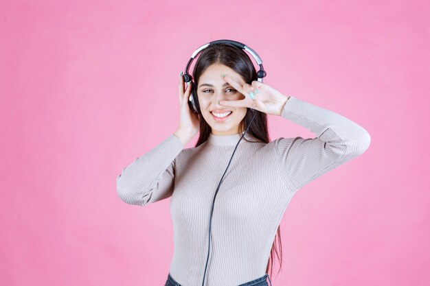 Girl with headphones listening the music and showing peace sign