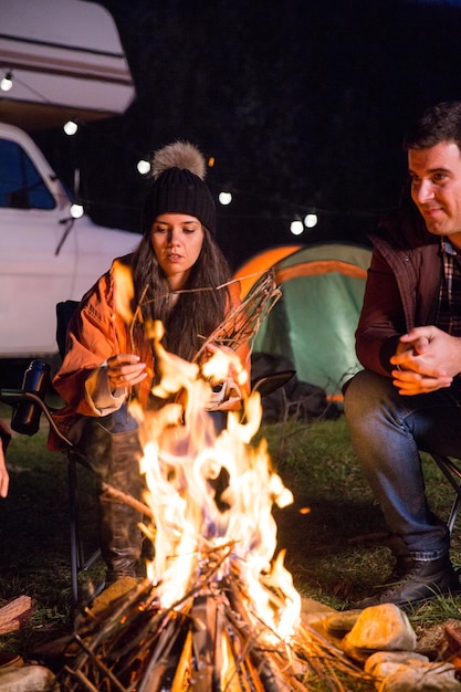 Free photo girl with her friends relaxing together in camp site around camp fire in the mountains. retro camper van.