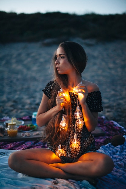 Free photo girl with light bulb chain sitting at the beach