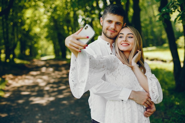 girl with light hair and a white dress is taking a photo in a sunny forest with her boyfriend