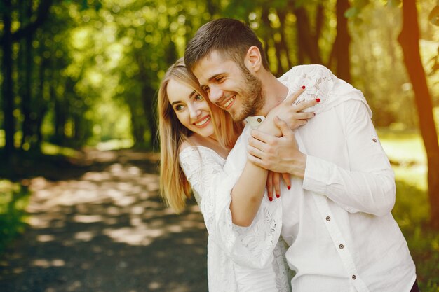 girl with light hair and a white dress is walking in a sunny forest with her boyfriend