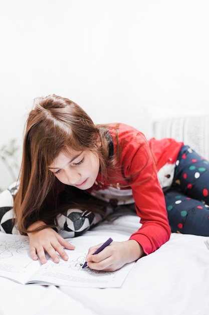 Girl with long hair drawing with crayon on bed