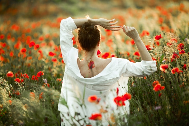 Free Photo girl with a naked back with a tattoo on it is holding hands over a head, and the beautiful poppies field