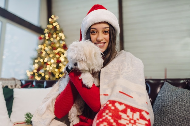 A girl with a small dog in her arms sits on the couch on New Year's Eve.