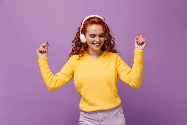 Free photo girl with wavy hair dances in headphones on lilac wall