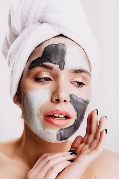 Girl without makeup does her morning routine on white wall. Lady uses clay mask to improve skin.