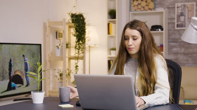 Free photo girl working on laptop from home office. girl taking a sip of coffee.