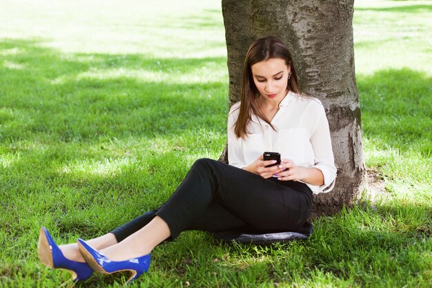 Girl works with her phone sitting under the tree