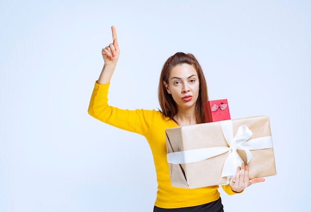 Girl in yellow shirt holding gift boxes and pointing up.