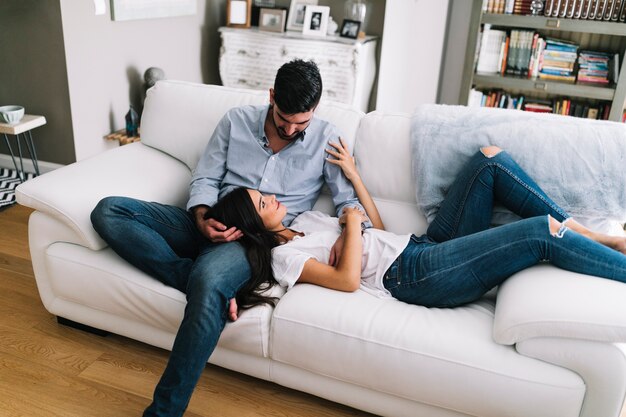 Girlfriend lying on man's lap sitting over white sofa at home