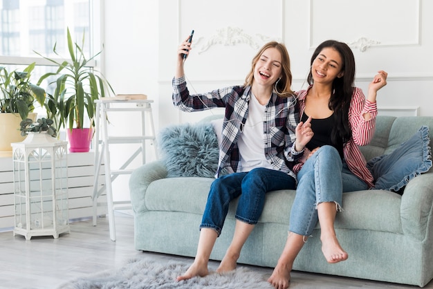 Girlfriends listening to music with headphones sitting on couch