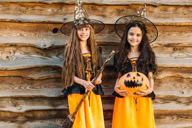 Free photo girls in halloween costumes with broom and pumpkin looking at camera