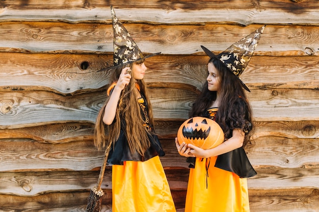 Free Photo girls in halloween costumes with broom and pumpkin looking at each other