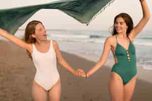 Free photo girls holding each other's hand flying scarf in the air at beach