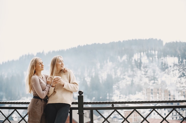 Girls in light clothes. Winter coffee on balcony. Happy women together.