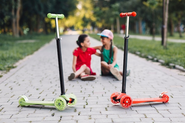 Free photo girls sitting behind the push scooters on walkway in the park