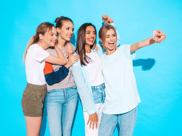 Free photo girls taking selfie self portrait photos on smartphone.models posing near blue wall in studio,female showing positive face emotions