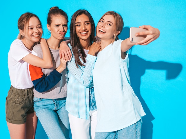 Free photo girls taking selfie self portrait photos on smartphone.models posing near blue wall in studio,female showing positive face emotions