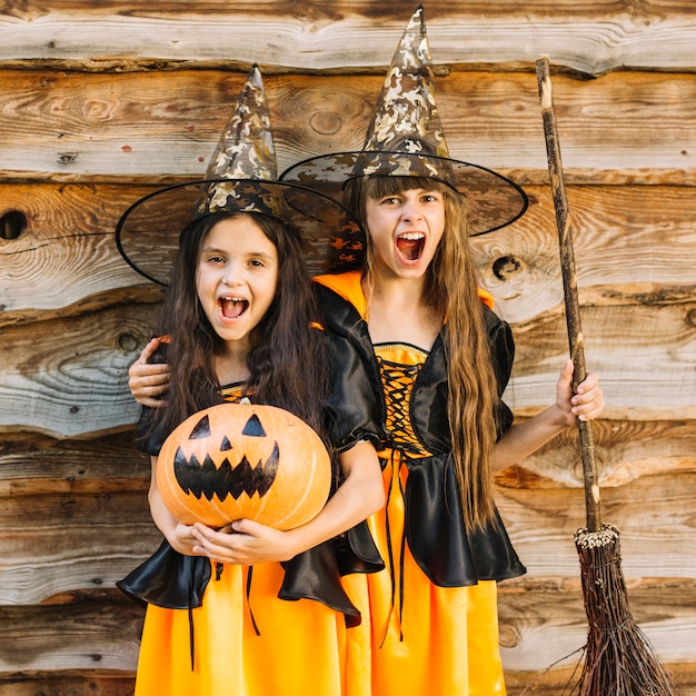 Girls in witch costumes making faces holding broomstick and pumpkin 