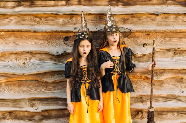 Girls in witch costumes making faces on wood background 