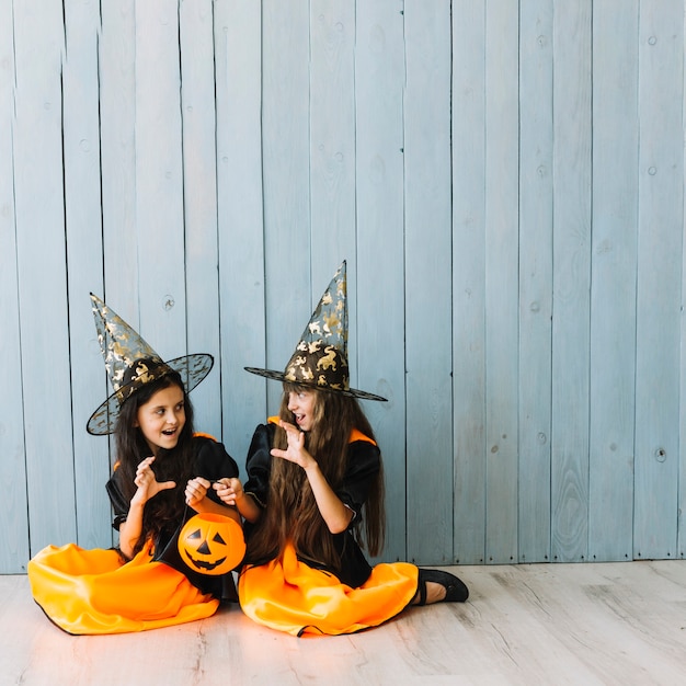 Free photo girls in witch costumes sitting on floor doing scary gestures