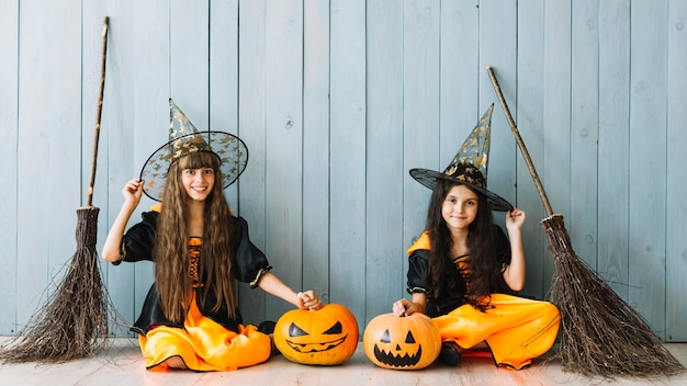 Free photo girls in witch costumes sitting with pumpkins and brooms