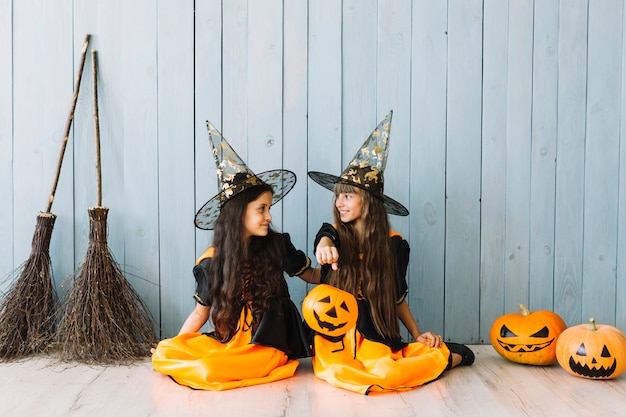 Free photo girls in witch suits and pointy hats holding halloween basket sitting on floor