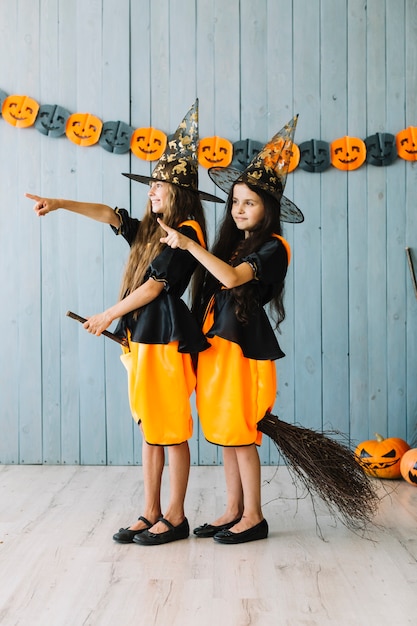 Free photo girls in witch suits sitting on broom pointing away