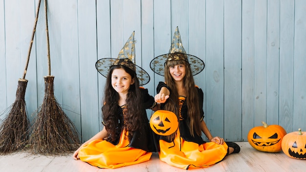 Girls in witch suits sitting on floor holding Halloween basket and smiling