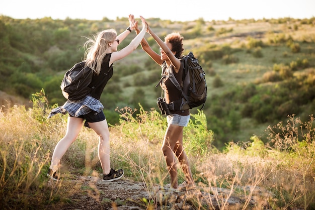 Free photo girls with backpacks smiling, giving highfive, traveling in canyon