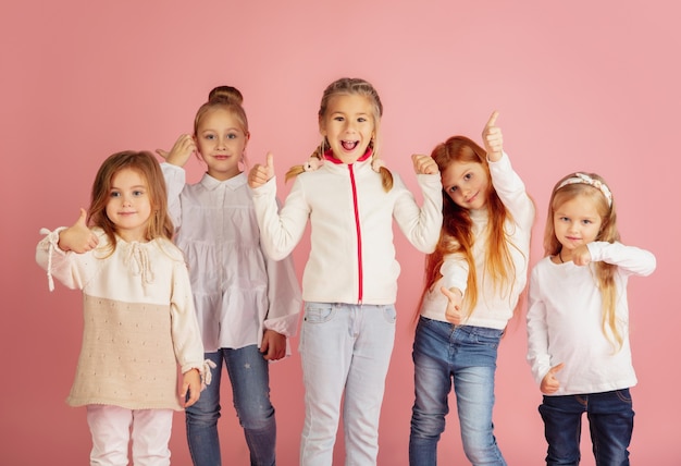 Giving and getting presents on Christmas holidays. Group of happy smiling children having fun, celebrating isolated on pink studio background. New Year 2021 meeting, childhood, happiness, emotions.