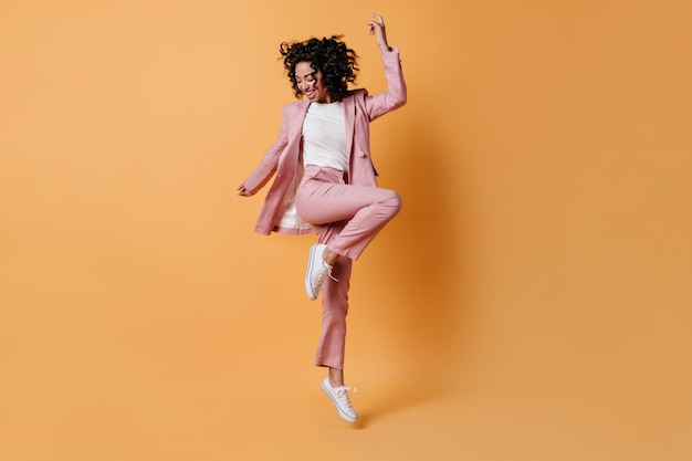 Free Photo glad curly girl jumping on yellow background full length view of happy lady in pink suit