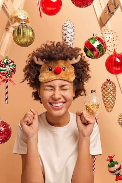 Free Photo glad dark skinned woman with curly bushy hair raises clenched fists and celebrates success prepares for celebrating christmas wears casual clothing poses 