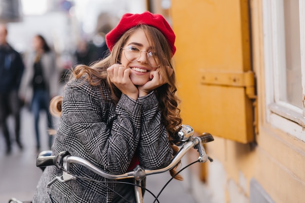 Free photo glad shy girl with brunette hair posing on blur city background in autumn day