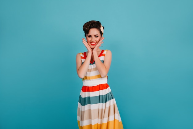 Free photo glad young woman in bright dress touching face. studio shot of charming pinup girl with elegant hairstyle.