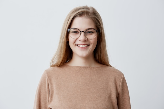 Free photo glad young woman with blonde straight hair and eyeglasses on, having gentle smile being happy to meet with her boyfriend. student female smiling into camera rejoicing her success at university.