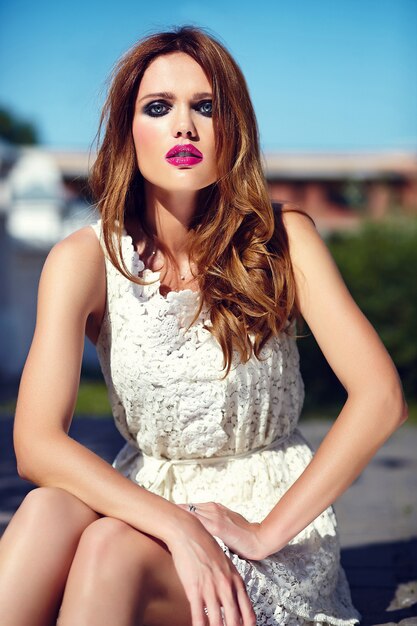 Glamor beauty portrait of beautiful sensual Caucasian young woman model with evening makeup in white summer dress posing on the street