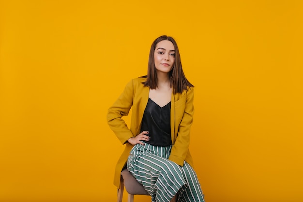 Free photo glamorous female model with straight hair sitting on chair. indoor portrait of stunning young woman in trendy yellow jacket.