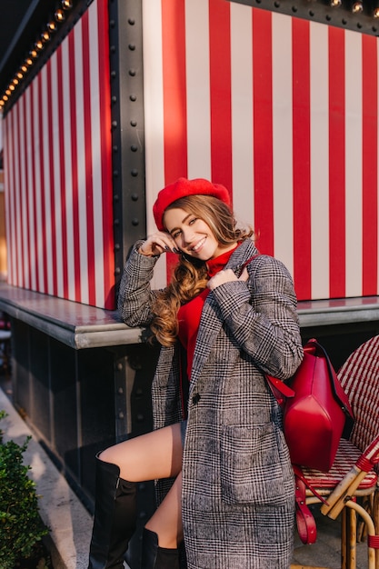 Free Photo glamorous girl in fashionable tweed coat sitting on the street with pretty smile