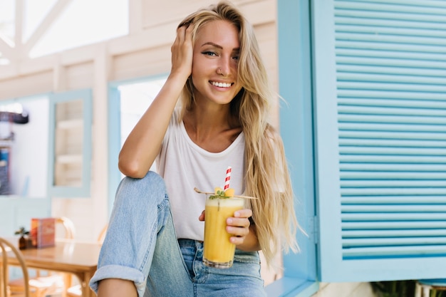 Free photo glamorous long-haired lady drinking cocktail with pleasure. photo of positive european woman holding glass of cold beverage.