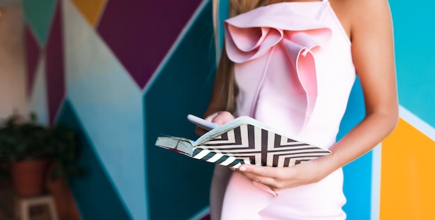 Glamorous woman in elegant pink dress holding notebook and smartphone