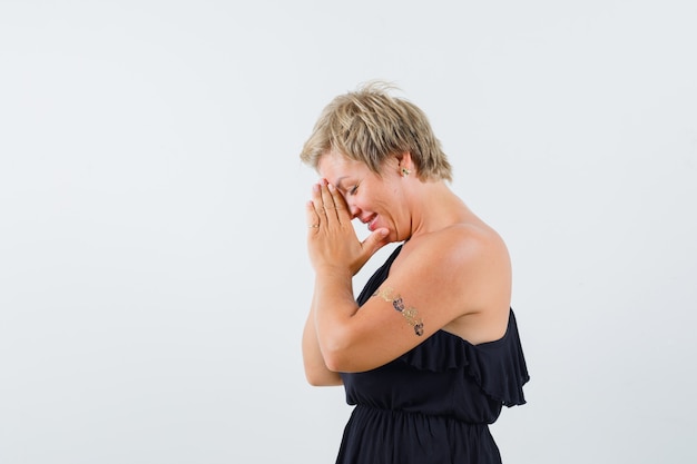 Free photo glamorous woman holding combined hands on her forehead while wishing in black blouse .